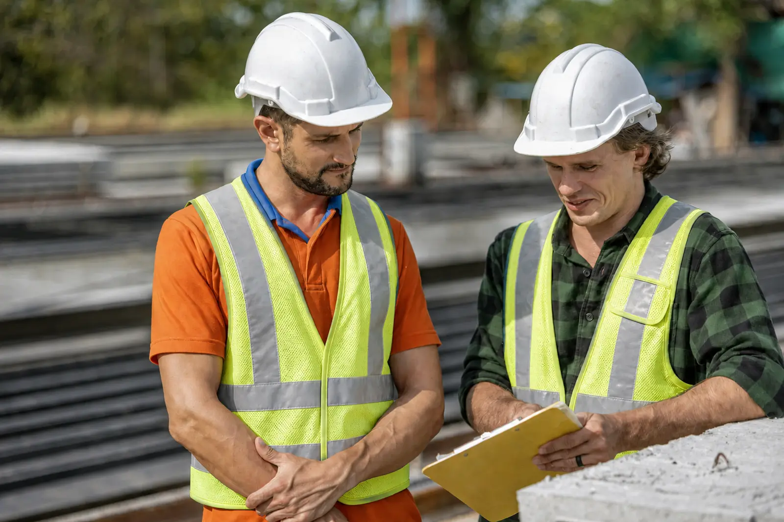 Two construction professionals in lime high-visibility vests and white helmets reviewing project plans together.