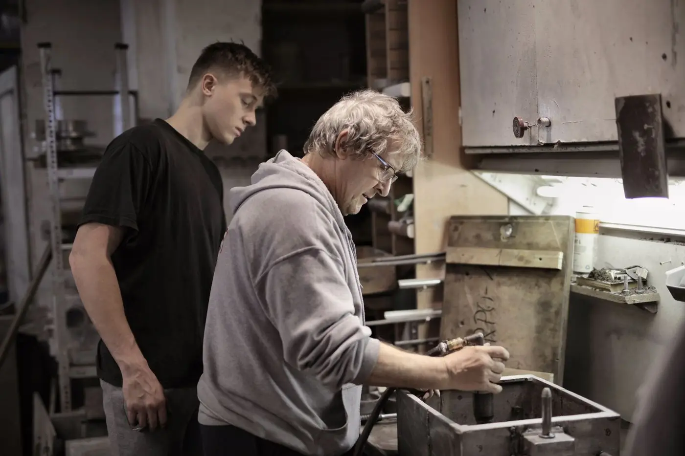 An experienced tradesperson guiding an apprentice at a workshop bench.