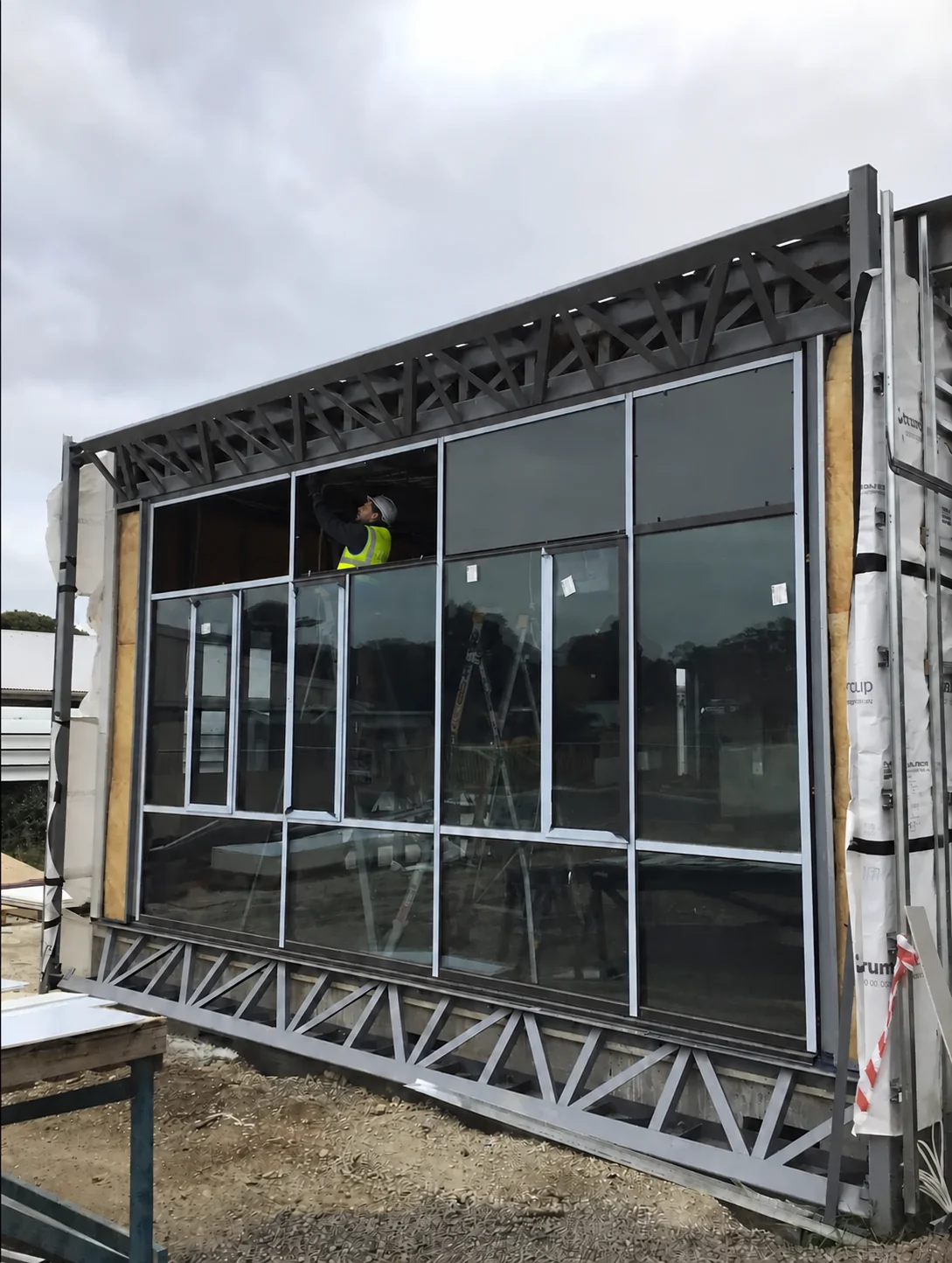 A glazier in a yellow reflective vest fitting a commercial glass facade.