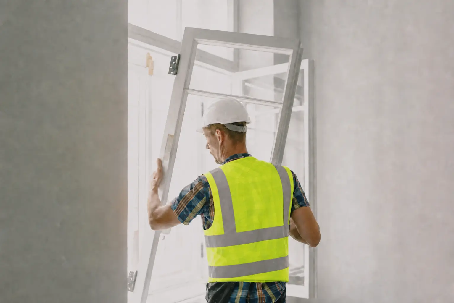 An installer in a lime high-visibility vest fitting a replacement window