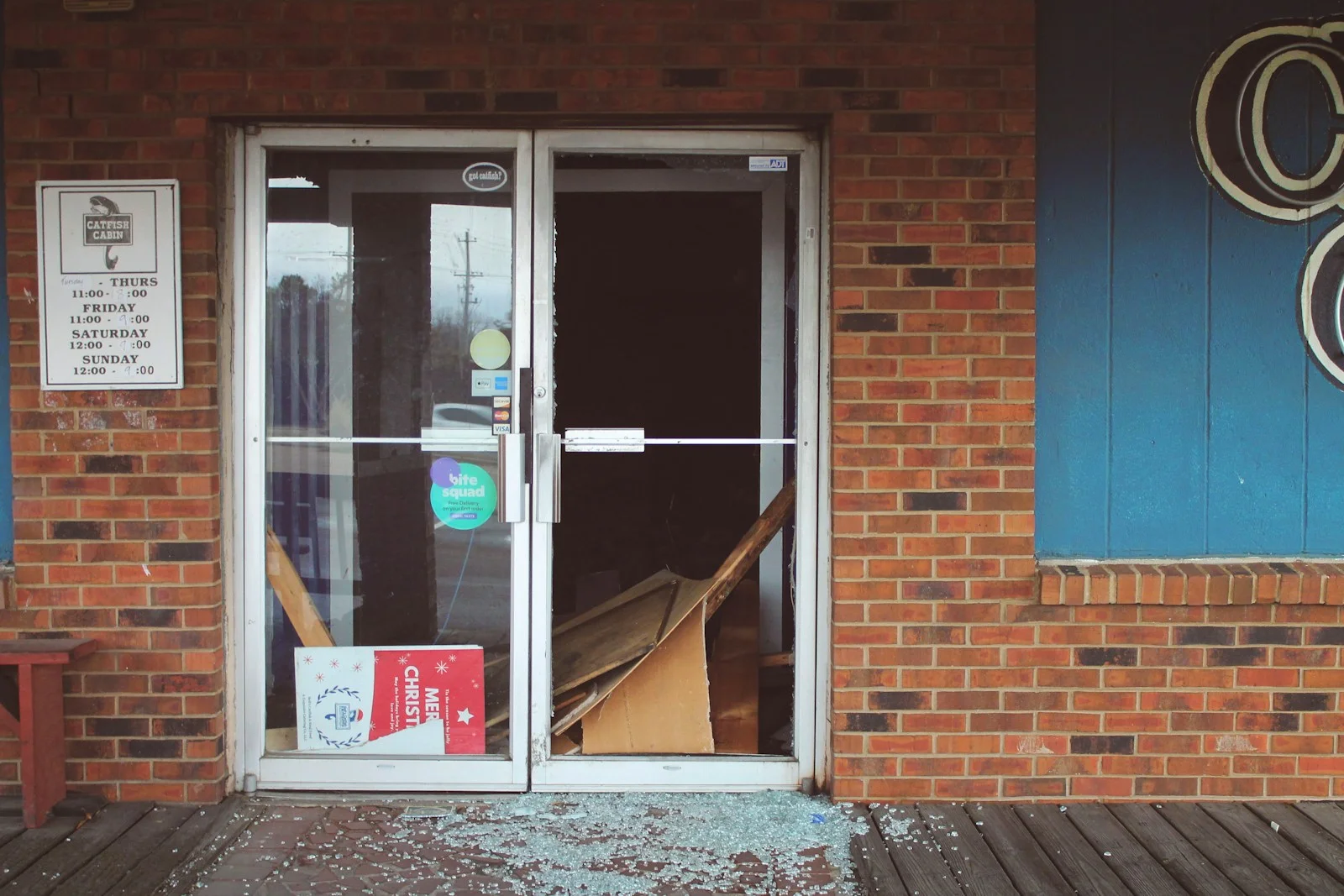 A shopfront with a smashed glass entrance door and shattered glass scattered across the ground.