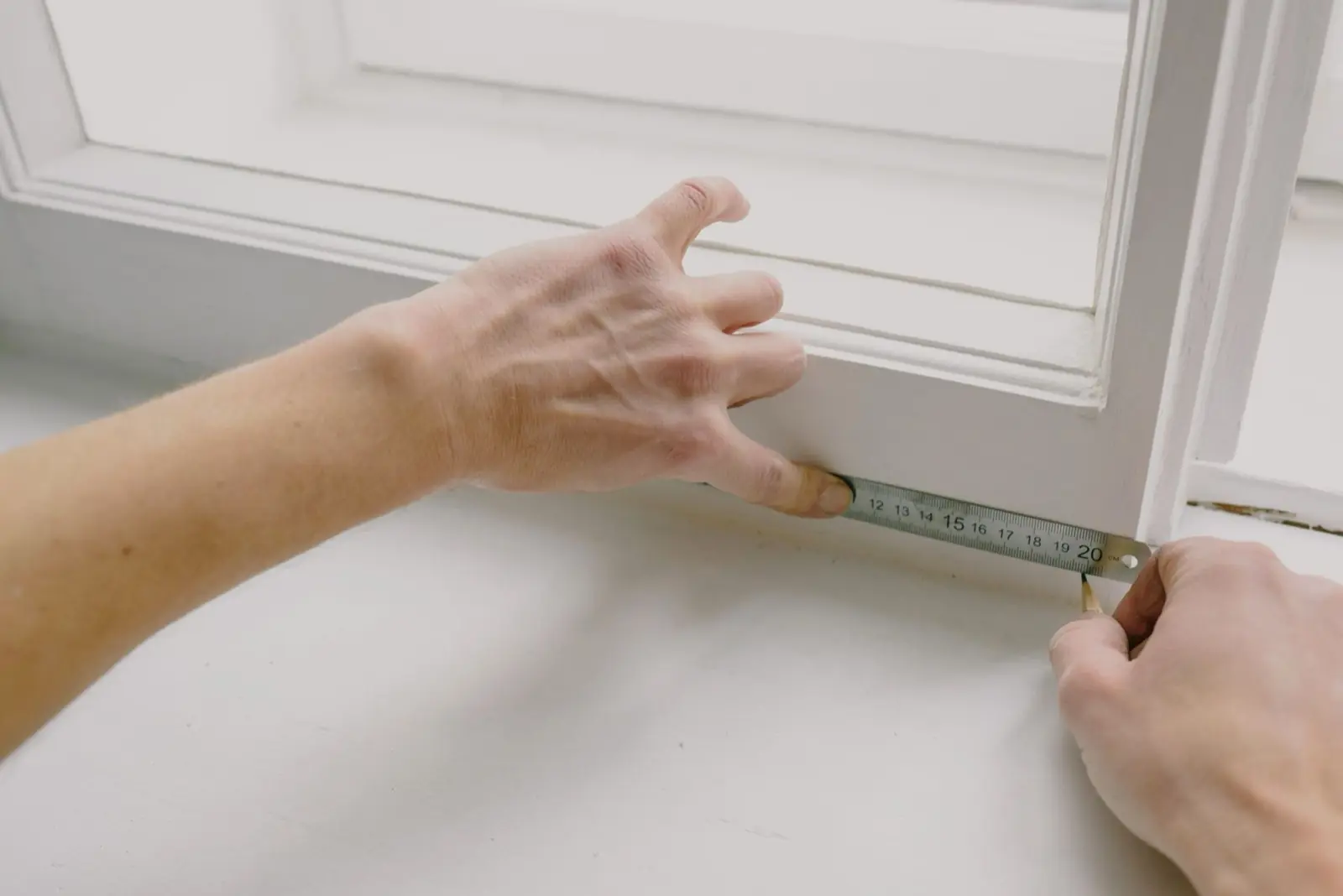 Hands measuring the width of a window frame.